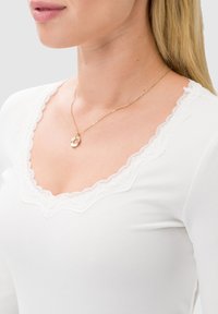 Biały, prążkowany top z dekoltem wykończonym koronką. Posiada dopasowany krój i długie rękawy, w połączeniu z delikatnym złotym naszyjnikiem z zawieszką.