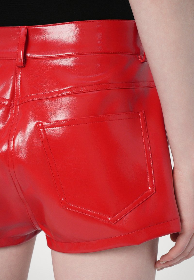 Shorts en simili cuir rouge avec une finition brillante, dotés d'une poche arrière et de coutures détaillées, coupés au-dessus de la mi-cuisse.