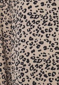 Beiger Stoff mit einem schwarzen Leopardenmuster, das verschiedene Größen von Flecken aufweist, mit einer glatten Textur und weicher Erscheinung.