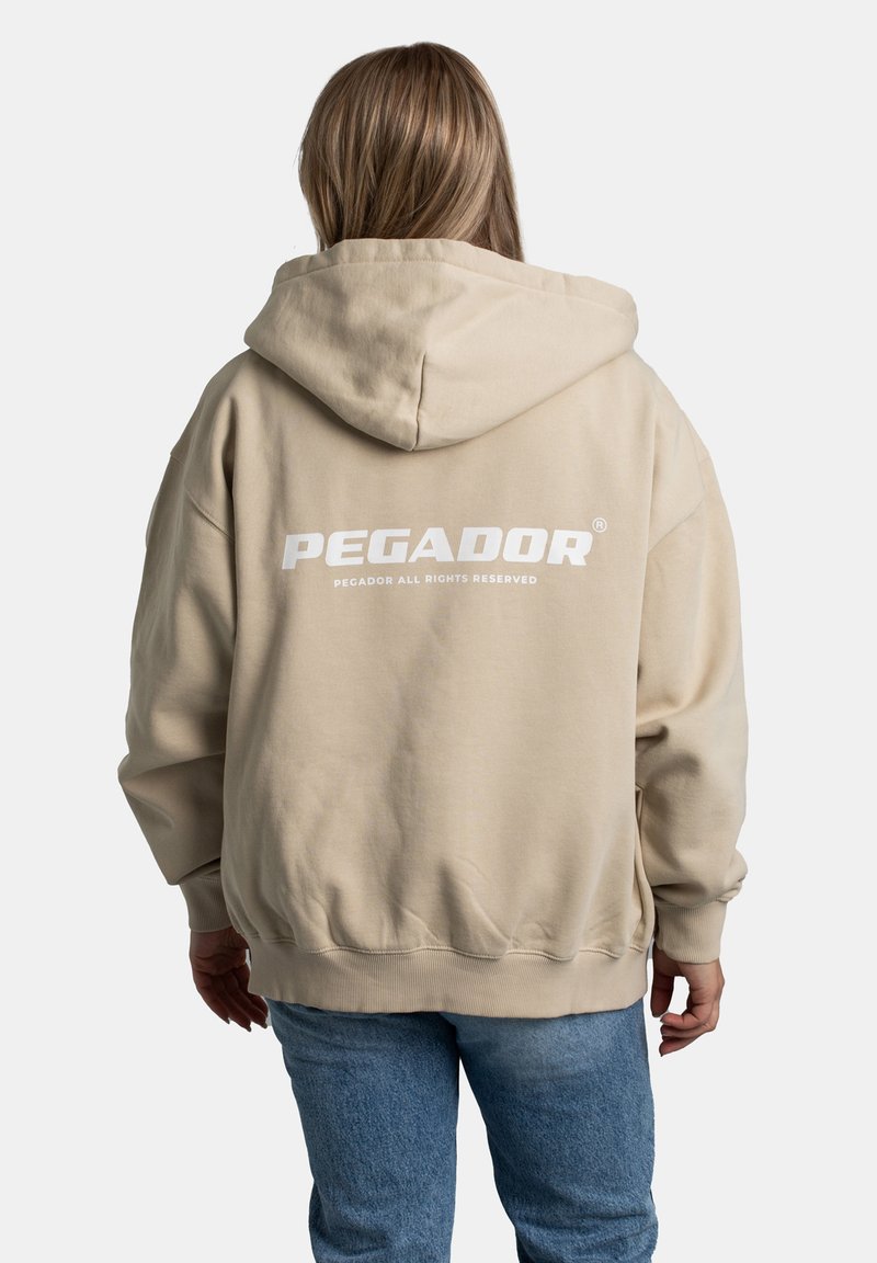 Beige oversized hoodie met een trekkoord capuchon. Voorzien van witte logo-tekst "PEGADOR" en "PEGADOR ALL RIGHTS RESERVED" op de achterkant. Zachte stof.