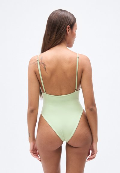 Μονόχρωμο μαγιό σε ανοιχτό πράσινο χρώμα, με λεπτές ρυθμιζόμενες τιράντες, ψηλές πλαγιές και λεία, ελαστική υφή. Χωρίς εμφανή σχέδια ή μεταλλικά στοιχεία.