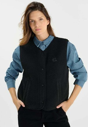 Black fleece vest with a rounded collar, front buttons, and side pockets. Worn over a light blue denim shirt.