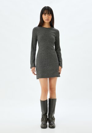 Robe en maille côtelée à manches longues de couleur gris foncé, silhouette ajustée. Portée avec des bottes noires jusqu'au genou ornées de boucles. Texture lisse.
