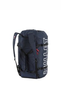 Sac de sport navy en tissu durable, avec des bretelles noires réglables, des accents de fermeture éclair rouges et un grand logo blanc sur le côté.