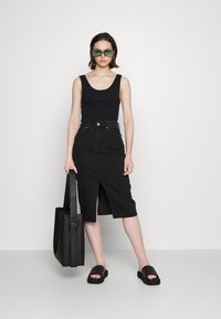 Top preto de alças, saia midi de ganga preta com fenda frontal, sandálias plataforma pretas e óculos de sol verdes. Bolsa tote preta com detalhe de fivela.