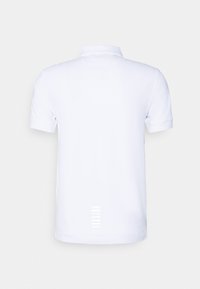 Polo blanc à manches courtes montré de dos avec un design sobre et de petites bandes réfléchissantes près de l'ourlet.