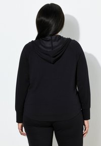 Černá mikina s kapucí vyrobená z měkké tkaniny s volným střihem. Má klokaní kapsu, dlouhé rukávy a jednoduchý design bez ozdob.