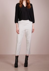 Zwart V-hals top met losse pasvorm; witte taps toelopende broek; zwarte enkellaarsjes met dikke hakken; gladde texturen; minimalistisch ontwerp.