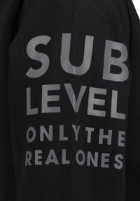 Schwarzes Sweatshirt mit großen grauen Aufdruck: "SUB LEVEL ONLY THE REAL ONES." Weicher Stoff, standardmäßiges Design ohne weitere Akzente.