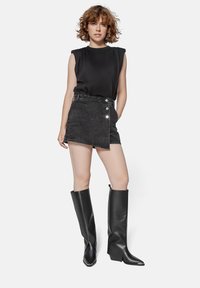 Black sleeveless top with shoulder padding, paired with a gray denim skirt featuring a side button closure and black knee-high heeled boots.