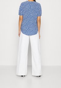 Haut bleu à manches courtes avec un motif floral blanc, assorti à un pantalon blanc ample et des chaussures à talons hauts.