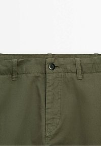 Ceinture de pantalon vert olive avec une fermeture à bouton noir, passants pour ceinture et coutures apparentes sur un fond uni.