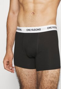 Schwarze Baumwoll-Boxershorts mit einem weißen elastischen Bund, auf dem der Text "ONLY&SONS" steht. Glatte Textur, enganliegendes Design, mittellange Schnittform.