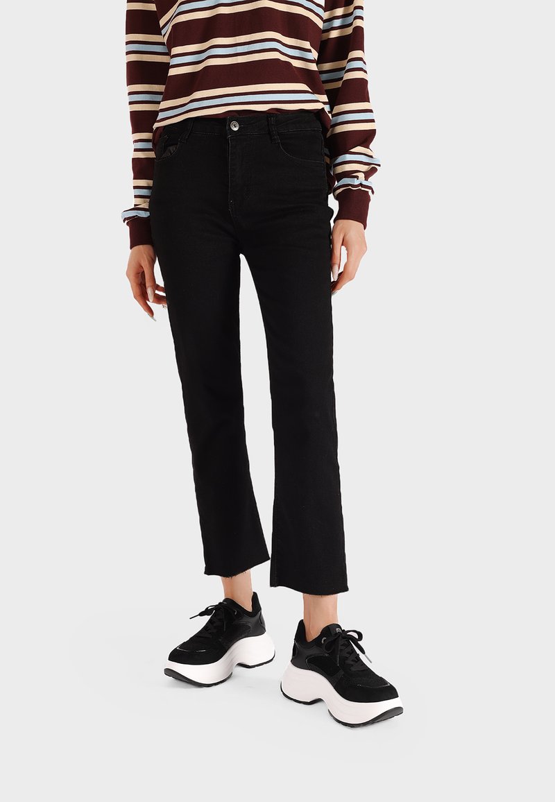 Jeans neri a vita alta con taglio dritto, abbinati a una maglietta a maniche lunghe a righe e a sneakers chunky bianche e nere. Texture liscia.