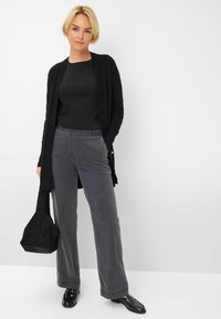 Zwarte open cardigan, nauwsluitend zwart topje, grijze wijde broek met een brede pijp en voorzakken, en zwarte instappers. Klein zwart tasje met een gestructureerd ontwerp.