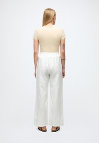 Beige figursydd t-shirt, vita vida byxor och sandaler. Mjukt tyg och elastisk midjeresår på byxorna. Bakifrån sett av outfiten.