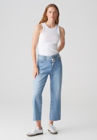 Lichtblauwe denim wide-leg jeans met een trekkoord in de taille, gecombineerd met een aansluitend wit tanktop en witte sneakers. Soepele textuur, casual stijl.