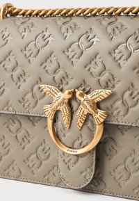 Borsa a tracolla in pelle beige con motivi in rilievo, dotata di una chiusura in metallo dorato con due uccelli. Include una tracolla in catena attorcigliata.