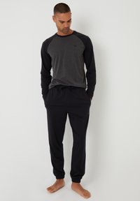 Top gris de manga larga con mangas raglán negras, combinado con pantalones negros ajustados. La tela parece suave; los pantalones tienen puños y cinturilla elásticos.