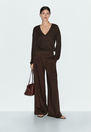 Bruin geribd gebreid V-hals trui gecombineerd met hoge taille, brede pantalon in een bijpassende bruine tint. Accessoires zijn onder andere een kleine bruine tas.