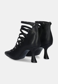 Zapatos de tacón alto de cuero negro con punta afilada, que presentan diseños calados, acentos circulares y un cierre de cremallera en la parte posterior.