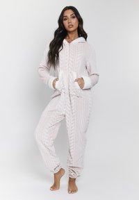 Fleece'owy kombinezon w miękkim beżu, z teksturą w warkocze, długimi rękawami, przednim zamkiem i kieszeniami z przodu. Rękawy wykończone są białym sztucznym futrem.