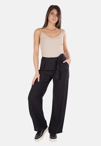 Canotta beige a coste e pantaloni neri a gamba larga con vita legata, caratterizzati da un tessuto morbido e da una vestibilità comoda. Sneakers nere completano il look.