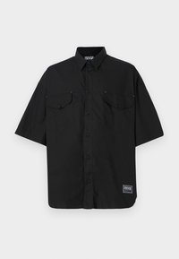 Black short-sleeve button-up shirt made from cotton, featuring two chest pockets and a logo label on the bottom right. Smooth texture.