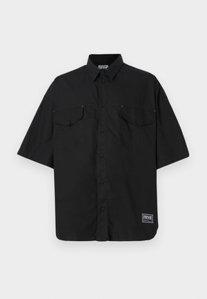 Schwarze kurzärmlige Button-up-Hemd aus Baumwolle, mit zwei Brusttaschen und einem Logolabel unten rechts. Glatte Textur.