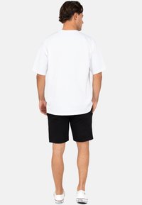 Witte T-shirt met korte mouwen en zwarte shorts. Het T-shirt heeft een ronde hals en een ontspannen pasvorm. De shorts zijn knielang met een effen ontwerp en zakken.