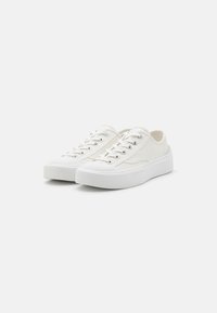 Witte canvas sneakers met een ronde neus, vetersluiting en een gestructureerd zijpaneel. Voorzien van een dikke witte rubberen zool.