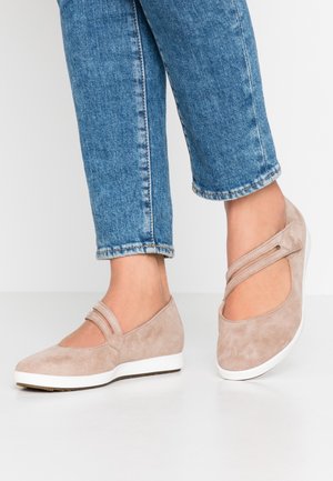 Chaussures plates en suède beige avec des découpes sur les côtés et deux détails de sangles, présentant une semelle en caoutchouc blanc et une texture lisse. Pantalons cropped en denim visibles.