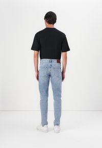 Camiseta negra de manga corta combinada con jeans ajustados de color azul claro. Zapatillas blancas visibles. Los jeans tienen un parche trasero de cuero color marrón.