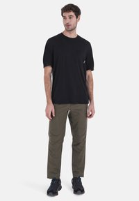 Black short-sleeve t-shirt with a chest pocket, paired with olive green stretch trousers featuring knee panels and black athletic shoes.