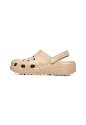 Zueco beige con puntera redondeada, orificios de ventilación laterales y una correa trasera. Presenta una parte superior texturizada y una suela gruesa acanalada.
