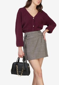 Bordeaux strikket cardigan med v-hals og perleknapper, kombineret med en ternet wrap-skirt og en lille sort håndtaske med en guldkæde.