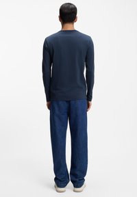 Marineblaues Langarm-T-Shirt mit rundem Ausschnitt, kombiniert mit locker sitzender blauer Jeans und beigen Sneakern. Strukturierter Stoff, lässiges Design.