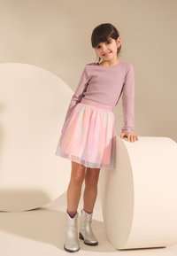 Light purple long-sleeve top with a fitted design, paired with a pastel pink, shimmery tulle skirt and silver ankle boots.
