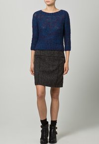 Suéter azul texturizado de punto con mangas tres cuartos, combinado con una falda gris ajustada. Botines negros completan el conjunto.