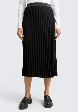 Zwarte geplooide rok met een gestructureerde tailleband, gemaakt van lichtgewicht stof; knielange ontwerp. Gecombineerd met stevige zwarte loafers.