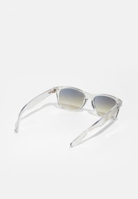 Ochelari de soare tip cat-eye, cu lentile gri cu gradient, cadru din plastic transparent și brațe subțiri ce au accente subtile de metal.