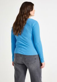Maglietta a maniche lunghe e righe di colore blu con un design aderente, abbinata a jeans grigi a vita alta, con dettagli di tasche posteriori standard.