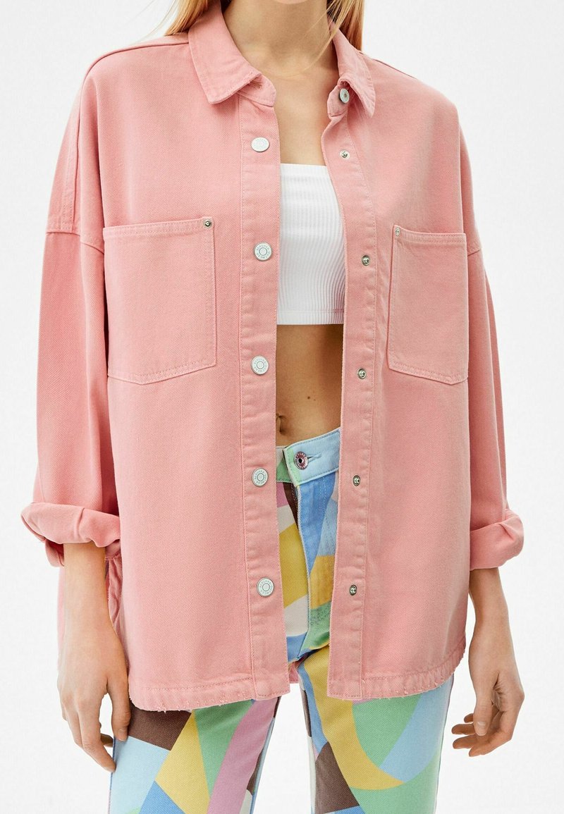 Rosa denimskjorta med krage, långa ärmar och två framfickor. Har silvriga knappar och en avslappnad passform.