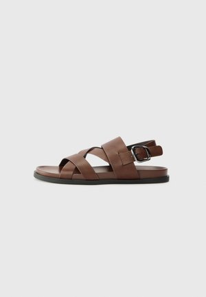 Bruine leren sandalen met kruisbanden, verstelbare gesp, platte zool en een gladde textuur. Minimalistisch ontwerp in een neutrale kleur.