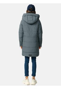 Gray hooded puffer jacket with quilted design, extending to mid-thigh. Paired with blue jeans and light-colored sneakers.