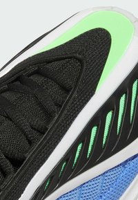 Zbliżenie czarnego trampka z zielonymi akcentami, białą podeszwą środkową i niebieskimi detalami z siateczki na boku i w rejonie palców.