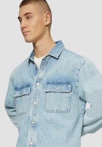 Jasnoniebieska koszula dżinsowa z zapinanym przodem, kołnierzykiem i dwoma kieszeniami na piersi. Charakteryzuje się wyblakłą teksturą i srebrnymi guzikami.