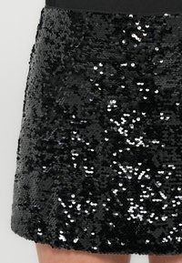 Mini-jupe noire en sequins avec une coupe ajustée, recouverte de sequins serrés créant une surface brillante et texturée.