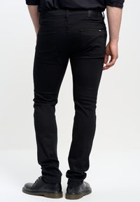 Jeans de mezclilla negros con un ajuste slim, que cuentan con dos bolsillos traseros y una etiqueta de cuero en la cinturilla. Combinados con zapatos de vestir negros.