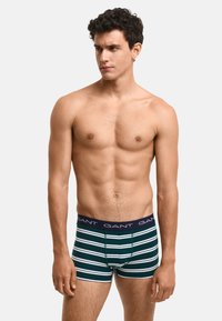 Zielone bokserki w ciemnej tonacji z białymi poziomymi paskami, z jednolitą granatową gumką w talii z logotypem "GANT". Dopasowany fason.